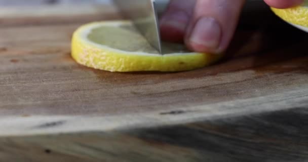 Een man snijdt de schijfjes citroen in twee helften voor presentatie op een houten achtergrond. 4k video — Stockvideo