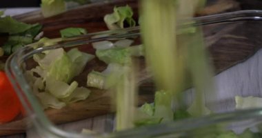 Bir adam marul dilimlerini şeffaf bir tabağa yavaş çekimde atar..