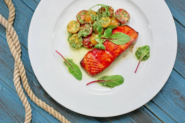 Serving plate grilled salmon with vegetables, Basil, tomatoes and sauce. On wooden blue old table background