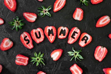 Taze çilek dilimlerinin üst görüntüsü kaba alçı yüzeyine yerleştirilmiş yaz yazılarını oluşturan harflerle.