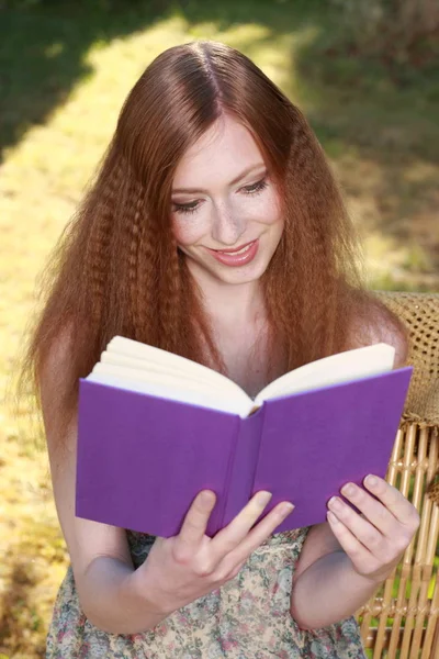 Rood harige vrouw in zomertuin lezen van een boek — Stockfoto