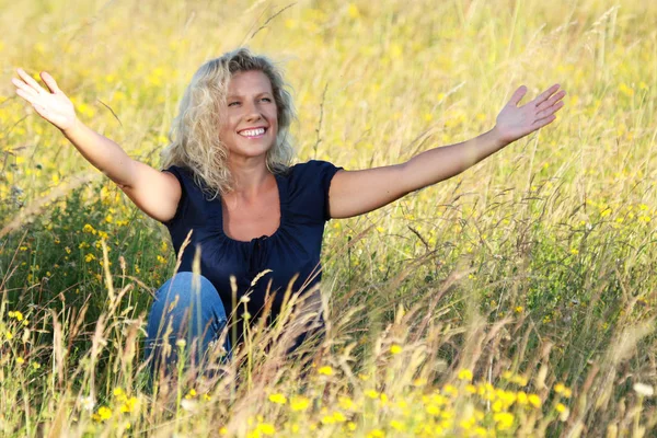 Happy mature woman spreading her arms in a meadow — Stock Photo, Image