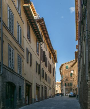 Siena, İtalya - 10 Kasım 2017. Açık mavi gökyüzü güneşli bir günde dar sokakları ve yüksek binalar üzerinde yürüyen insanlar