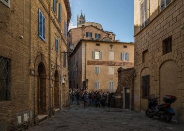 Siena, İtalya - 10 Kasım 2017. Güneşli bir günde dar sokakları ve yüksek binalar üzerinde yürüyen insanlar