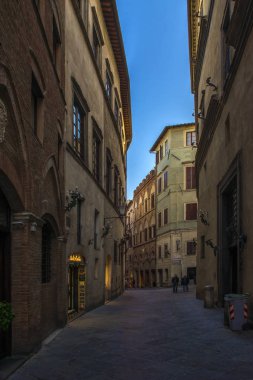 Siena, İtalya - 10 Kasım 2017. Dar sokaklar ve alacakaranlıkta erken morgning üzerinde yüksek binalar üzerinde yürüyen insanlar