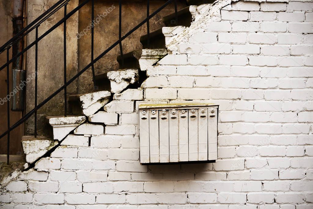 White multi devision mailbox hanging on white brick wall under stairway