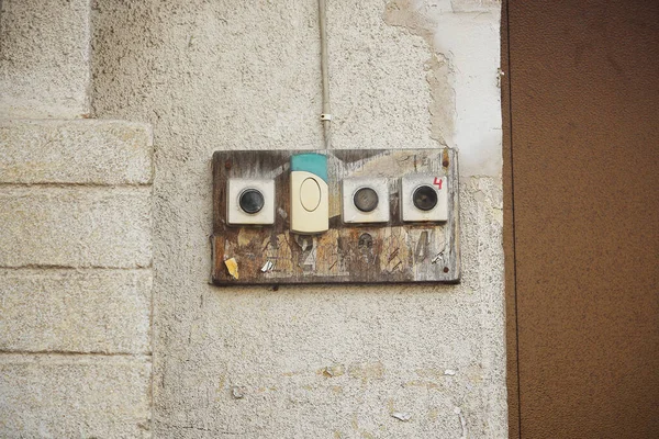 Four old door bell buttons on concrete wall near brown door