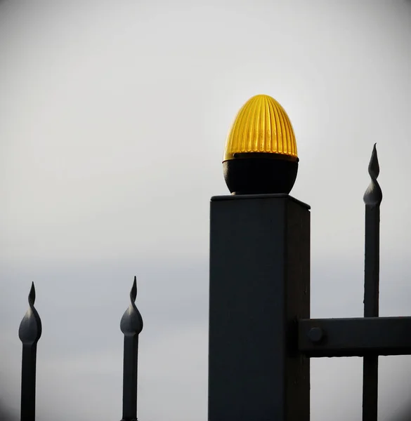 Orange light bulb on black metal fence on white sky background