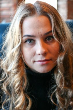 Uzun kıvırcık saçlı ve altın takılı güzel bir kadın. Bir kafede poz vermek, büyük küpeler, gülüşmeler, flörtler..