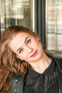 Siyah elbise giyen zarif sarışın kız bir kafede dinleniyor. Reklam, moda, ticari tasarım. Siyah deri ceketli, uzun kıvırcık dudaklı, parlak kırmızı dudaklı ve tırnaklı bir kafedeki kız..