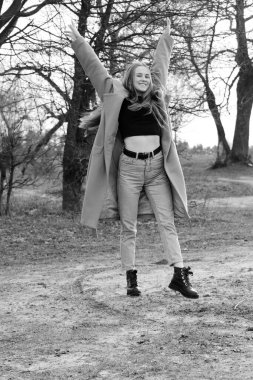 Açık havada mutlu, çarpıcı sarışın kızın moda portresi. Güzel gülümseme. Uzun açık renk saçlı. Şık bir ceket giyiyor. Neşeli ve neşeli bir kadın. Doğal bir arazide, kuru bir sazlığın ve bir gölün yanında yürümek. siyah ve beyaz