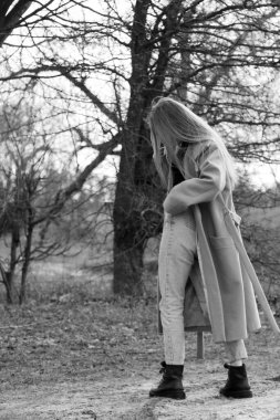 Açık havada mutlu, çarpıcı sarışın kızın moda portresi. Güzel gülümseme. Uzun açık renk saçlı. Şık bir ceket giyiyor. Neşeli ve neşeli bir kadın. Doğal bir arazide, kuru bir sazlığın ve bir gölün yanında yürümek. siyah ve beyaz