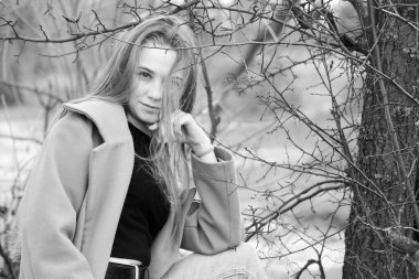 Açık havada mutlu, çarpıcı sarışın kızın moda portresi. Güzel gülümseme. Uzun açık renk saçlı. Şık bir ceket giyiyor. Neşeli ve neşeli bir kadın. Doğal bir arazide, kuru bir sazlığın ve bir gölün yanında yürümek. siyah ve beyaz