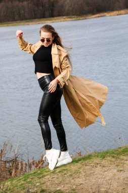 Açık havada mutlu, çarpıcı sarışın kızın moda portresi. Güzel gülümseme. Uzun açık renk saçlı. Şık bir ceket giyiyor. Neşeli ve neşeli bir kadın. Doğal bir arazide yürümek, kuru bir sazlığın yanında ve güneşli bir günde bir göl..