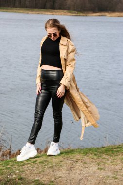 Açık havada mutlu, çarpıcı sarışın kızın moda portresi. Güzel gülümseme. Uzun açık renk saçlı. Şık bir ceket giyiyor. Neşeli ve neşeli bir kadın. Doğal bir arazide yürümek, kuru bir sazlığın yanında ve güneşli bir günde bir göl..