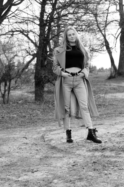 Outdoors lifestyle fashion portrait of happy stunning blonde girl. Beautiful smile. Long light hair. Wearing stylish coat. Joyful and cheerful woman. walk on a natural landscape, near a dry reed and a lake. black and white