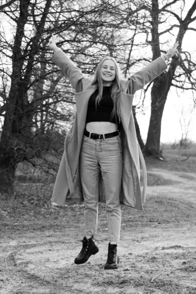 Outdoors lifestyle fashion portrait of happy stunning blonde girl. Beautiful smile. Long light hair. Wearing stylish coat. Joyful and cheerful woman. walk on a natural landscape, near a dry reed and a lake. black and white