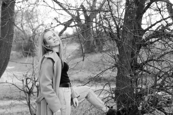 Outdoors lifestyle fashion portrait of happy stunning blonde girl. Beautiful smile. Long light hair. Wearing stylish coat. Joyful and cheerful woman. walk on a natural landscape, near a dry reed and a lake. black and white
