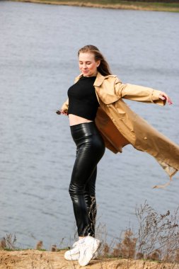 Açık havada mutlu, çarpıcı sarışın kızın moda portresi. Güzel gülümseme. Uzun açık renk saçlı. Şık bir ceket giyiyor. Neşeli ve neşeli bir kadın. Doğal bir arazide yürümek, kuru bir sazlığın yanında ve güneşli bir günde bir göl..