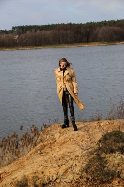 Açık havada mutlu, çarpıcı sarışın kızın moda portresi. Güzel gülümseme. Uzun açık renk saçlı. Şık bir ceket giyiyor. Neşeli ve neşeli bir kadın. Doğal bir arazide yürümek, kuru bir sazlığın yanında ve güneşli bir günde bir göl..