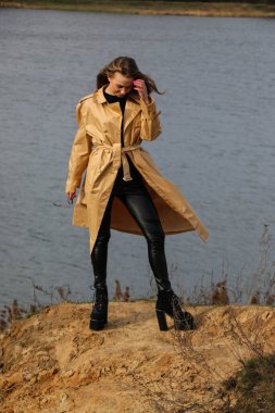 Açık havada mutlu, çarpıcı sarışın kızın moda portresi. Güzel gülümseme. Uzun açık renk saçlı. Şık bir ceket giyiyor. Neşeli ve neşeli bir kadın. Doğal bir arazide yürümek, kuru bir sazlığın yanında ve güneşli bir günde bir göl..