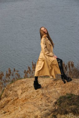 Açık havada mutlu, çarpıcı sarışın kızın moda portresi. Güzel gülümseme. Uzun açık renk saçlı. Şık bir ceket giyiyor. Neşeli ve neşeli bir kadın. Doğal bir arazide yürümek, kuru bir sazlığın yanında ve güneşli bir günde bir göl..