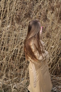 Açık havada mutlu, çarpıcı sarışın kızın moda portresi. Güzel gülümseme. Uzun açık renk saçlı. Şık bir ceket giyiyor. Neşeli ve neşeli bir kadın. Doğal bir arazide, kuru bir sazlığa ve göle yakın yürümek.