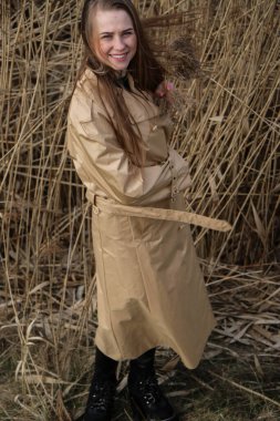 Açık havada mutlu, çarpıcı sarışın kızın moda portresi. Güzel gülümseme. Uzun açık renk saçlı. Şık bir ceket giyiyor. Neşeli ve neşeli bir kadın. Doğal bir arazide, kuru bir sazlığa ve göle yakın yürümek.