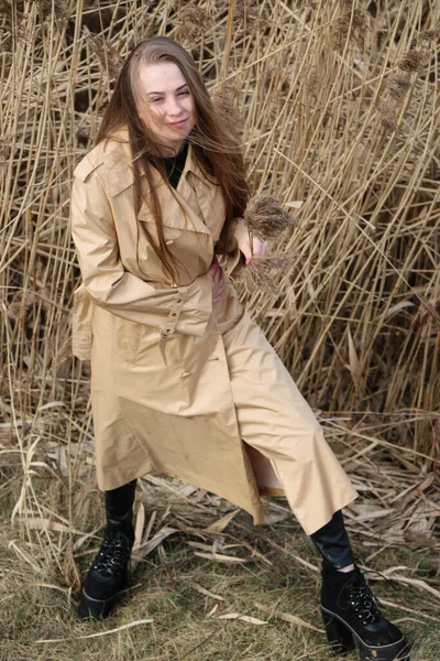 Outdoors lifestyle fashion portrait of happy stunning blonde girl. Beautiful smile. Long light hair. Wearing stylish coat. Joyful and cheerful woman. walk on a natural landscape, near a dry reed and a lake
