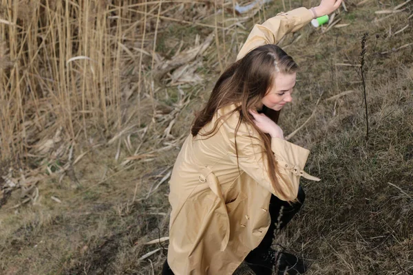 Outdoors lifestyle fashion portrait of happy stunning blonde girl. Beautiful smile. Long light hair. Wearing stylish coat. Joyful and cheerful woman. walk on a natural landscape, near a dry reed and a lake