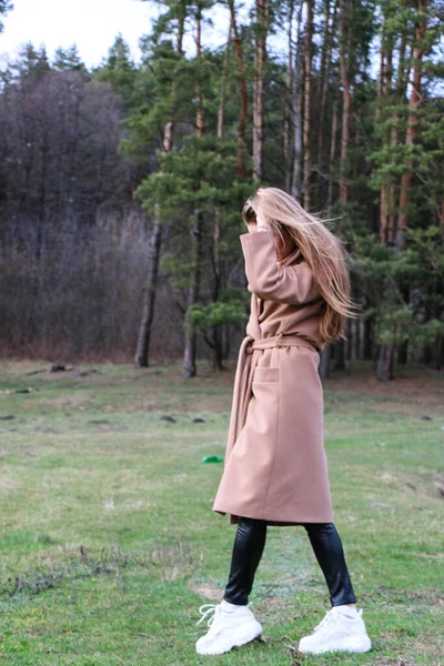 stock image beautiful girl, blonde with long hair, walks in the spring near the forest in a brown coat., serenity and freedom