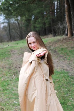 Güzel bir kız, sarışın, uzun saçlı, ilkbaharda ormanın yakınında kahverengi ceketli, dinginlik ve özgürlük içinde yürüyor.
