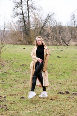 Güzel bir kız, sarışın, uzun saçlı, ilkbaharda ormanın yakınında kahverengi ceketli, dinginlik ve özgürlük içinde yürüyor.