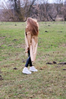 Güzel bir kız, sarışın, uzun saçlı, ilkbaharda ormanın yakınında kahverengi ceketli, dinginlik ve özgürlük içinde yürüyor.