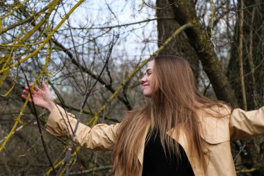 Dışarıdaki kameraya poz veren güzel bir genç kadın. Hızlı bir geçmiş. Açık havada. Kapatın. Kuru sazlığın ve mavi gölün yakınında güneşli bir günde. Kahverengi ceketli, uzun saçlı, güzel bir sarışın.