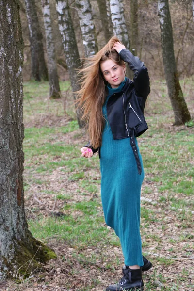 Vacker flicka, blond med långt hår, går på våren nära skogen i en brun rock — Stockfoto