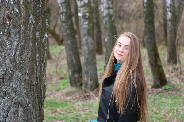 Hermosa chica, rubia con el pelo largo, camina en la primavera cerca del bosque en un abrigo marrón —  Fotos de Stock