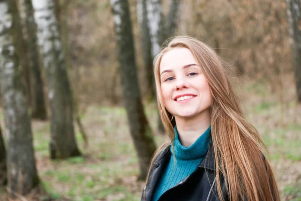 Bella ragazza, bionda con i capelli lunghi, passeggiate in primavera vicino alla foresta in un cappotto marrone — Foto Stock