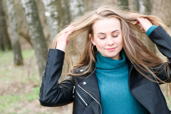 Bella ragazza, bionda con i capelli lunghi, passeggiate in primavera vicino alla foresta in un cappotto marrone — Foto Stock