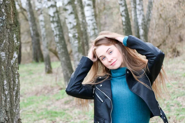 Schönes Mädchen, blond mit langen Haaren, spaziert im Frühling in der Nähe des Waldes im braunen Mantel — Stockfoto