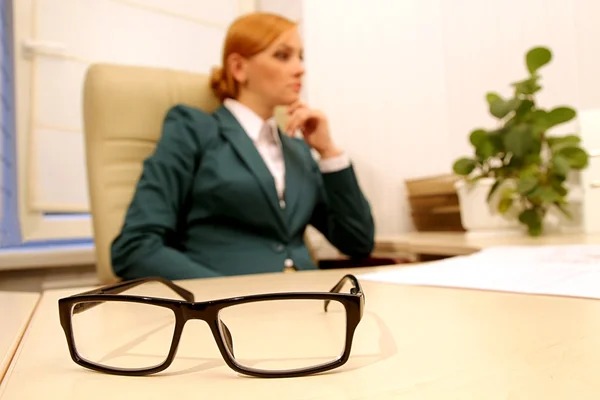 Brille im Vordergrund auf dem Schreibtisch vor nachdenklichem Hintergrund — Stockfoto