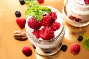 Sağlıklı kahvaltı - tatlı yoğurt, granola, çıkışları pul, reçel, ahududu, yaban mersini, fındık ve nane altın zemin üzerine yoğurt kavanozlara. 