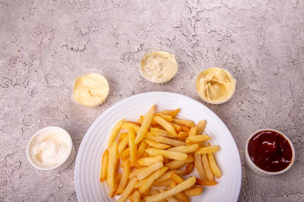 White plate of french fries chips potato and sauces on gry concr — Stock Photo, Image