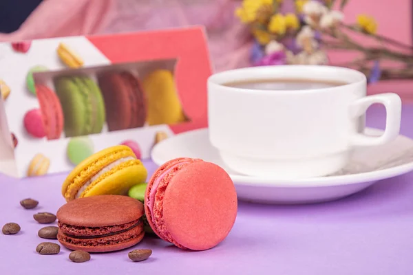 Macarons coloridos e xícara de café, grãos de café na violeta — Fotografia de Stock