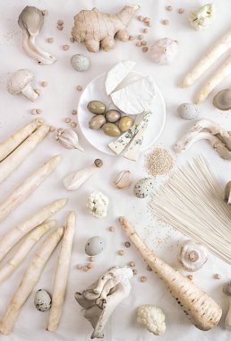 Bitki bazlı modern natürmort. Beyaz arka planda pişen çiğ vegan malzemeleri: kuşkonmaz, mantar, yumurta, erişte, peynir. Beyaz üzerine beyaz kavramı. Masraflar. Üst görünüm.