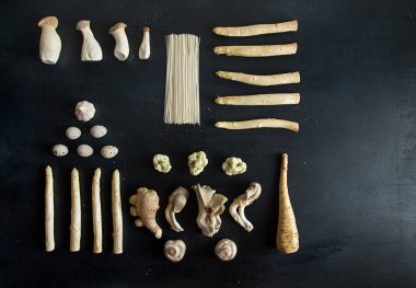Bitki bazlı modern natürmort. Siyah arka planda pişirmek için ham malzemeler: beyaz kuşkonmaz, mantar istiridye, karnabahar, erişte, sarımsak, yumurta ve siyah arka planda zencefil. Masraflar. Üst görünüm. Boşluğu kopyala.