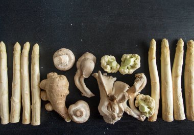 Bitki bazlı modern natürmort. Siyah arka planda pişirmek için ham malzemeler: beyaz kuşkonmaz, mantar istiridyesi, karnabahar ve siyah arka planda zencefil. Masraflar. Üst Manzara. Boşluğu kopyala.