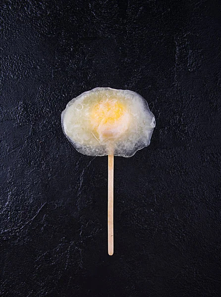 Frozen egg on wooden stick over on black background. Top view. Copy space