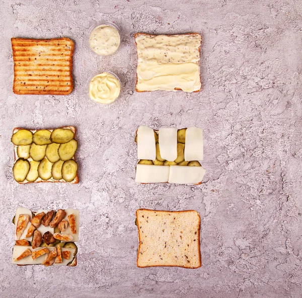 Step-by-step preparation sandwich with chicken meat, marinated cucumbers, mozzarella cheese and sauces over on grey concrete background. Geometric Layout Ingredients composition. Top view. Flat lay