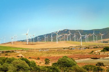 Rüzgar türbinleri, yenilenebilir yeşil enerji üretimi için güzel doğa manzarasında mavi gökyüzüne karşı tarım jeneratörleri üretiyor. Çevreye dost sanayi. Sürdürülebilir geliştirme teknolojisi kavramı.